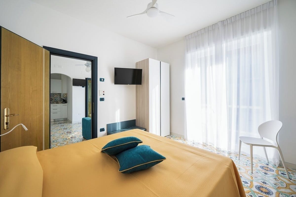 A hotel room with a bed, a TV, a wardrobe, and a view of the kitchen.