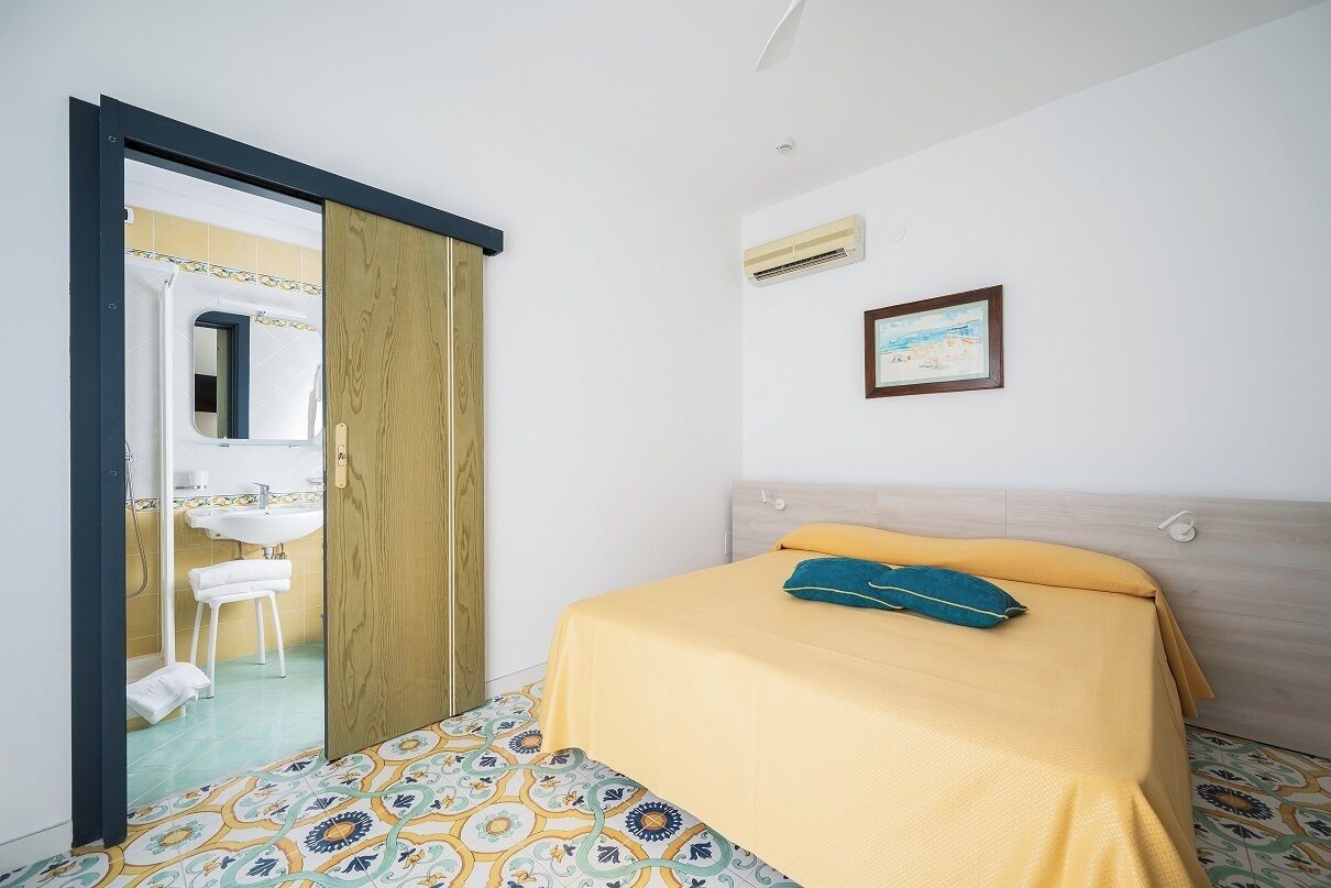 A bedroom with a bed, a wooden door, a bathroom with a sink, and a shower.