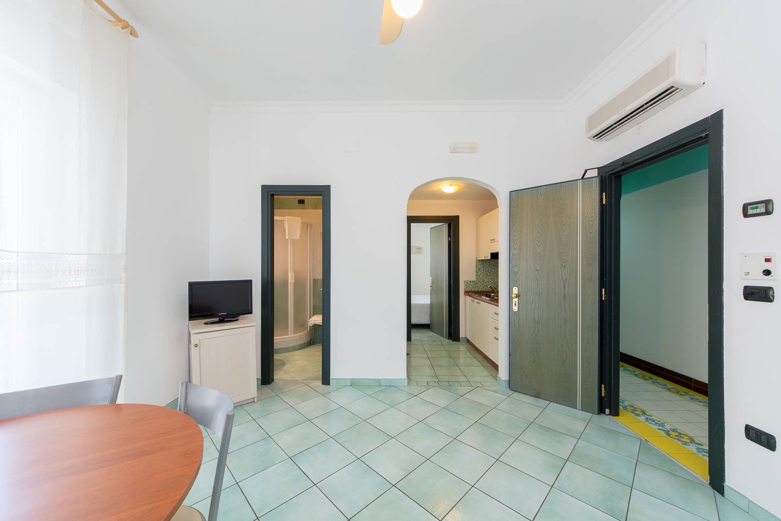 Habitación de hotel con una mesa de comedor de madera, televisión, zona de ducha y kitchenette.
