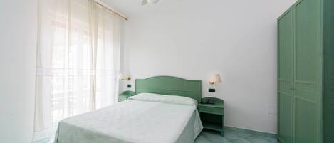 A single bed with a green headboard, two bedside tables with lamps, a ceiling fan, and a green wardrobe.