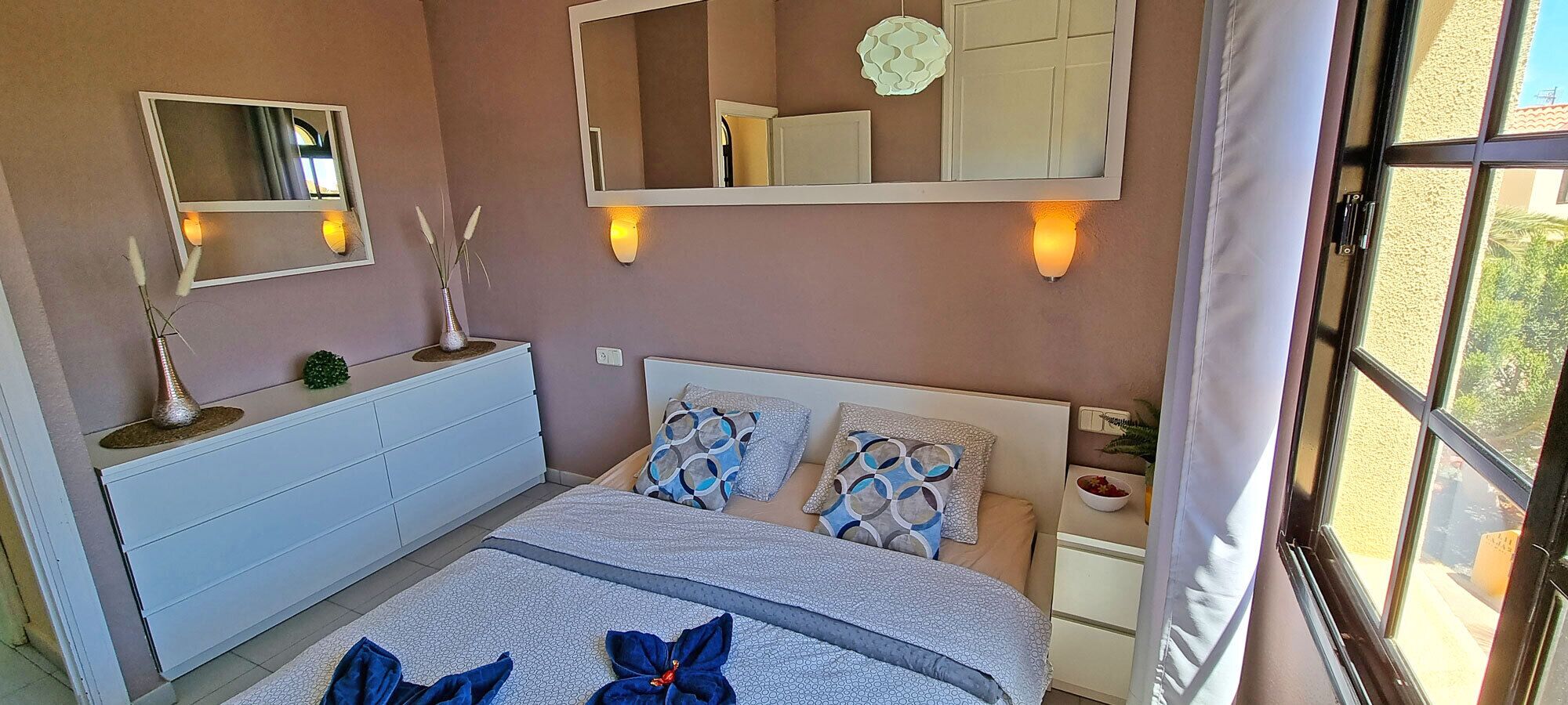 A bedroom with a bed, bedside tables, a dresser, and wall-mounted mirrors.