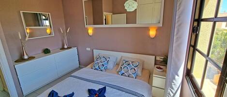 A bedroom with a bed, bedside tables, a dresser, and wall-mounted mirrors.