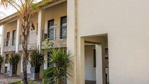 A building with a modern design, featuring a balcony on the second floor, potted plants, and a stone facade. - Luxury Apartment at Peo (Maun)