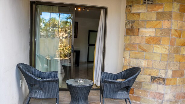 A patio with two wicker chairs and a small table, a sliding glass door, and a stone wall. - Luxury Apartment at Peo (Maun)