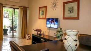 A living room with a television, framed pictures, a decorative vase, and a table with a remote control. - Luxury Apartment at Peo (Maun)