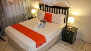 A neatly made bed with a white and orange blanket, two bedside lamps, and a small decorative item on the nightstand. - Luxury Apartment at Peo (Maun)
