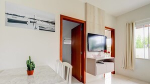 A modern living room with a dining table, a television mounted on a wooden cabinet, and a potted plant. - Origin Casa -2 Bedroom Beach House for up to 7 (Palhoça)