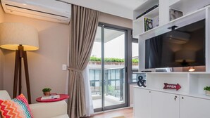 A modern living room with a sofa, a red side table, a lamp, a TV, and a sliding glass door to a balcony. - Na85b Modern Studio in the Best V. Madalena (São Paulo)
