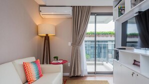 A modern living room with a white sofa, colorful pillows, a floor lamp, a small red table, and a TV on a white cabinet. - Na85b Modern Studio in the Best V. Madalena (São Paulo)