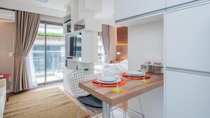 A modern, well-lit room with a dining table set for two, a TV mounted on a white wall, and a balcony with curtains. - Na85b Modern Studio in the Best V. Madalena (São Paulo)