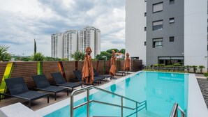 A rooftop pool with lounge chairs and umbrellas, surrounded by a wooden fence and modern buildings in the background. - Na85b Modern Studio in the Best V. Madalena (São Paulo)