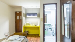 A compact hotel room with a wooden floor, a yellow desk with a microwave, a coffee maker, and a glass. A door leads to a bathroom with a toilet and a sink. - No1712 Fantástico a Poucos Metros da Paulista! (São Paulo)