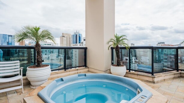 A rooftop terrace with a hot tub, two potted palm trees, and a city skyline view. - Ad404 Stylish Apartment in the Best Part of Itaim (São Paulo)