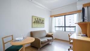 A modern, minimalistic living room with a sofa, a round table, and a TV on a wooden stand. - Tu705 Varanda e Muito Conforto na Al Lorena! (São Paulo)