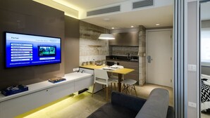 Une cuisine moderne avec un coin repas, un téléviseur fixé au mur affichant une interface NET TV et un canapé dans l’espace salon.