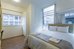 A hotel room with a bed, a window, a wardrobe, and a small table.