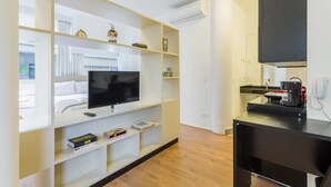 A modern hotel room with a flat-screen TV, built-in shelves, a black desk, and a large window.