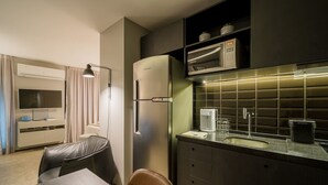 Une cuisine moderne équipée d’un four à micro-ondes encastré, d’un réfrigérateur et d’un évier avec un robinet en acier inoxydable. On y trouve également un coin repas avec une table et des chaises, ainsi qu’un téléviseur fixé au mur.