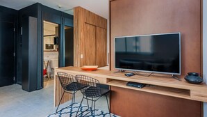 A modern living space with a TV, wooden furniture, and a kitchen area visible through an open door. - Ad604 Estúdio a 1 Quadra da Av. Paulista (São Paulo)