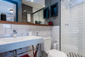Une salle de bain moderne avec un lavabo, des toilettes et une douche, le tout de couleur blanche. Deux miroirs à cadre noir sont accrochés au mur, et un panier rouge est posé sur le sol.