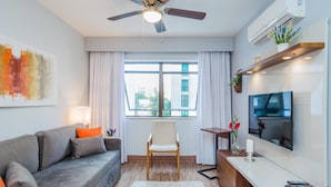 A modern living room with a grey sofa, a white chair, a TV mounted on the wall, and a ceiling fan.