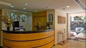 A reception area with a curved wooden desk, a receptionist, a small cart, and a window with a view of the street.