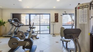 A gym with cardio machines, a weight bench, and a wall-mounted instructional poster. - Ce806 Flat Para 1 ou 2 Pessoas nos Jardins! (São Paulo)
