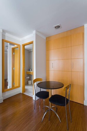 A room with a wooden floor, a round table with two chairs, and a wooden wardrobe. - Ce806 Flat Para 1 ou 2 Pessoas nos Jardins! (São Paulo)