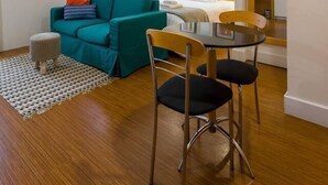 A modern hotel room with a teal sofa, a small round table with two chairs, a bed with white linens, and a large mirror. - Ce806 Flat Para 1 ou 2 Pessoas nos Jardins! (São Paulo)