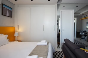 Quarto de hotel moderno com uma cama grande, uma escrivaninha, um sofá e um guarda-roupa.