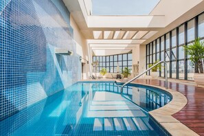 Una piscina interior con agua cristalina y azul, rodeada por un muro de azulejos y una terraza de madera.