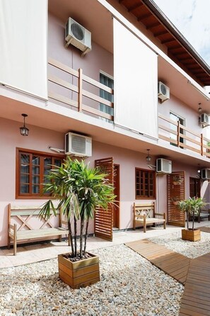 Un edificio de varios pisos con balcones, unidades de aire acondicionado, muebles de madera y plantas en macetas.