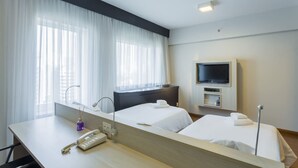 A hotel room with two beds, a TV, a desk with a phone, and a window with sheer curtains. - Me1211 Próximo à Paulista, na Bela Vista (São Paulo)