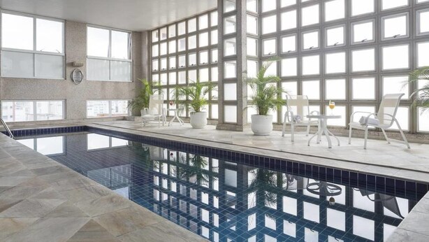 An indoor swimming pool with a tiled floor, large windows, and several potted plants. - Me1211 Próximo à Paulista, na Bela Vista (São Paulo)