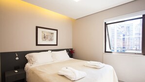 Siisti hotellihuone, jossa on huolitellusti pedattu sänky, yöpöytä lampun kanssa, seinällä oleva kehystetty kuva ja ikkuna, josta avautuu näkymä kaupunkiin.