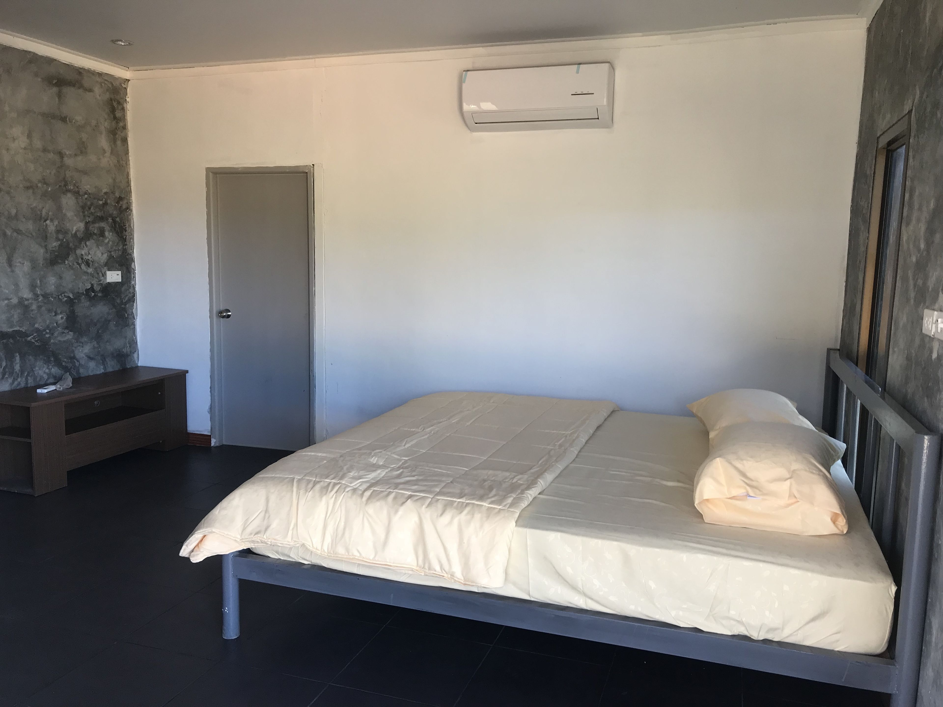 A bedroom with a bed, a nightstand, a door, and an air conditioning unit on the wall.