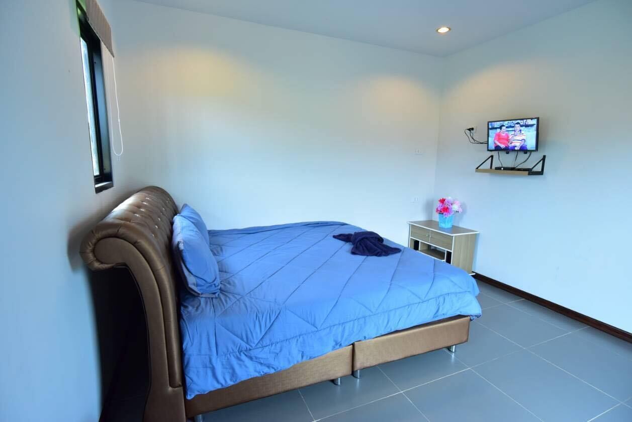 A bedroom with a bed, a TV on a stand, a nightstand, and a window.