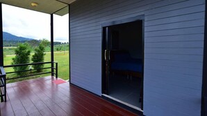 Quarto com porta de vidro deslizante que dá para uma varanda com vista para uma paisagem verde e montanhas.