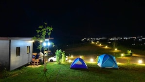 Um camping noturno com duas tendas, uma cabana pequena e um veículo estacionado por perto.