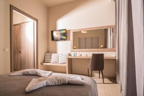 A hotel room with a bed, a desk with a chair, a television, and a bathroom with a mirror. - Petros Hotel (Zakynthos)