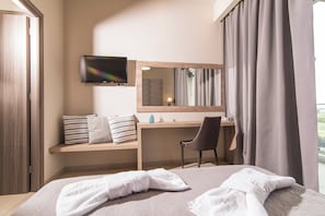 A hotel room with a bed, a desk, a chair, a TV, a mirror, and a window with curtains. - Petros Hotel (Zakynthos)