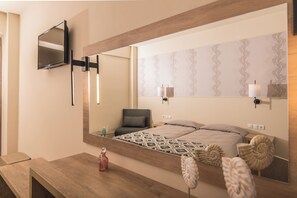 A hotel room with a large mirror, a bed with patterned bedding, a bedside table with a bottle, and a chair. - Petros Hotel (Zakynthos)