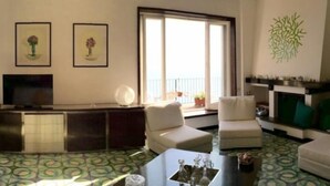 Un salon comprenant un canapé, des fauteuils, une table basse, un téléviseur et une cheminée. Deux tableaux encadrés ornent le mur, ainsi qu’un élément de décoration murale de couleur verte.