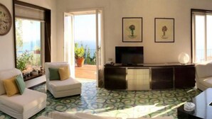 Un salon avec un canapé, un téléviseur et un balcon agrémenté de plantes en pot.