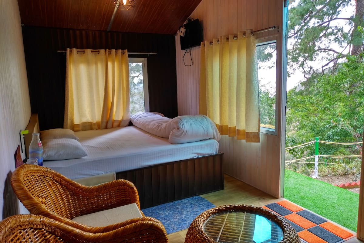 A bedroom with a bed, two windows with curtains, a television, and a view of the outdoors.