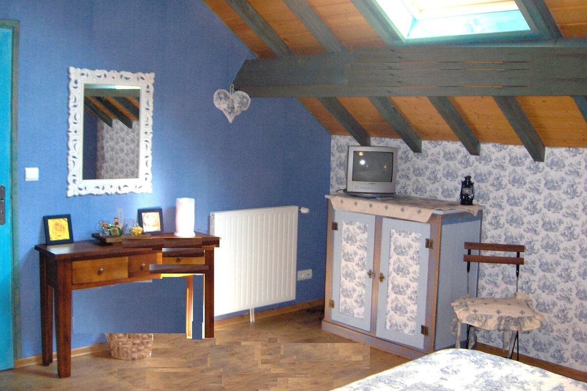 Un dormitorio con techo inclinado, un escritorio de madera, un televisor sobre un mueble y una silla.