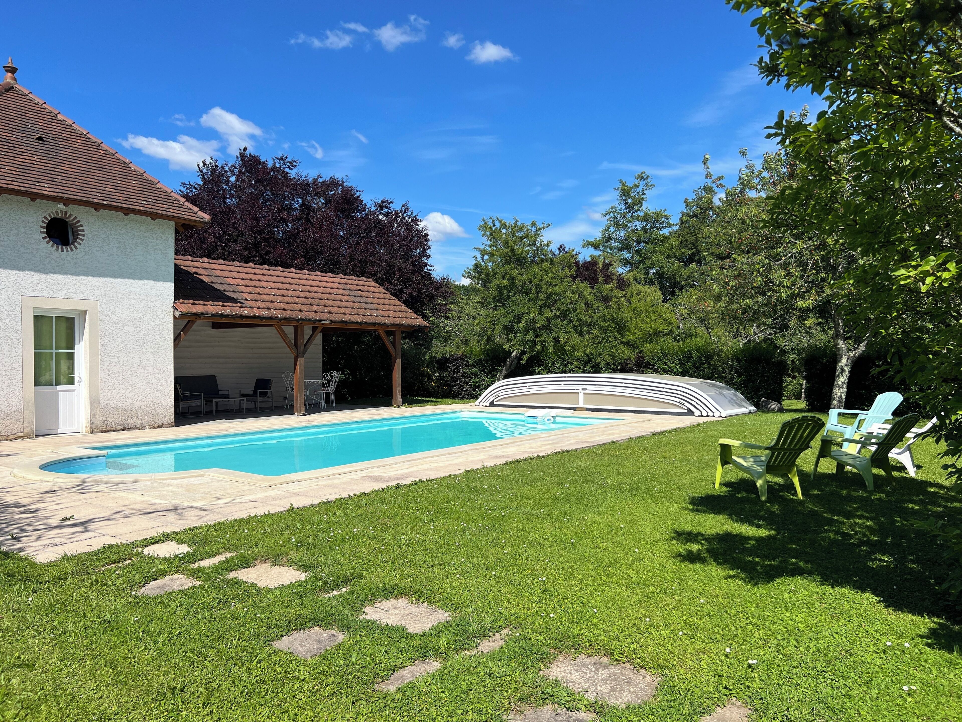Ein Garten mit Swimmingpool, überdachter Terrasse und Gartenmöbeln.