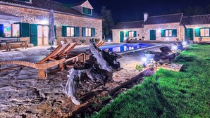 Un edificio de piedra con piscina, zona de estar exterior y jardín iluminado por la noche.