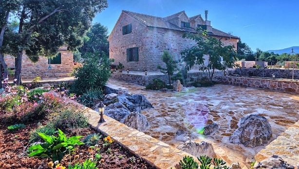 Un edificio de piedra con tejado de baldosas, rodeado de un jardín con diversas plantas y flores.