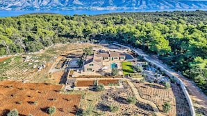 Vista aérea de una propiedad con un edificio central rodeado de jardines en terrazas y una zona boscosa.